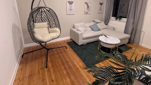 Een woonkamer met een hangstoel, een bank, een klein rond tafeltje en een potplant.