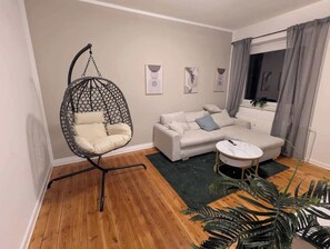 Ein Wohnzimmer mit Hängekorbschaukel, Sofa, kleinem runden Tisch und Blumentopf.