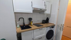 Een kleine keuken met witte kastjes, een houten aanrecht, een spoelbak, een wasmachine en een koffiezetapparaat.