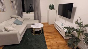 Een woonkamer met een witte bank, een ronde salontafel, een televisie, een plant en een radiator.