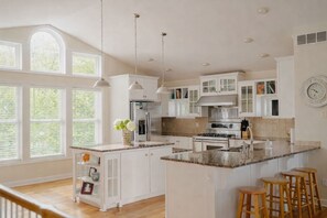 Una cocina amplia con armarios blancos, una isla grande y vistas al exterior a través de amplios ventanales.