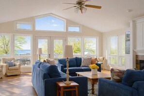 A spacious living room with a large blue sofa, a wooden coffee table, and a ceiling fan. - Aqua Breeze/Lakefront, Hot Tub, Fire Pit, 3 Decks (Michigan City)