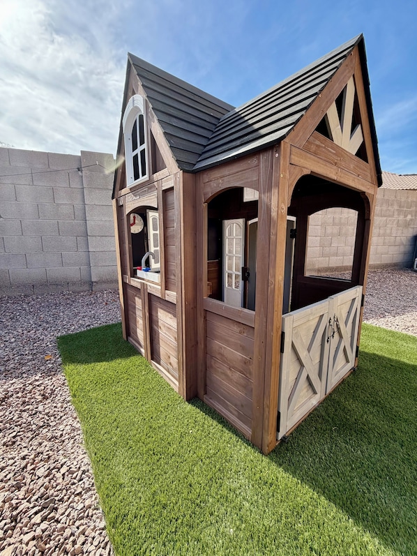 Une cabane en bois pour enfants, avec un toit incliné, une fenêtre et une porte.