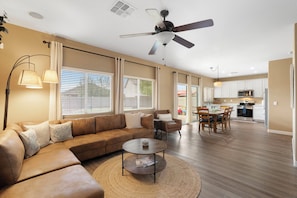 A spacious living room with a brown leather sofa, a coffee table, and a ceiling fan. - Desert Family Oasis, Pool, Spa & Kids’ Paradise (Avondale)