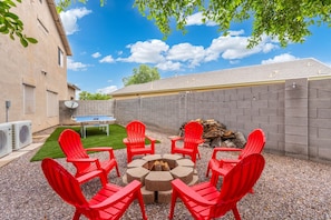 An outdoor seating area with red chairs around a fire pit, a ping pong table, and a building with a brick wall and windows. - Desert Family Oasis, Pool, Spa & Kids’ Paradise (Avondale)