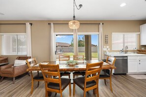 A dining area with a wooden table and chairs, a hanging light fixture, and a view of the backyard through a sliding glass door. - Desert Family Oasis, Pool, Spa & Kids’ Paradise (Avondale)