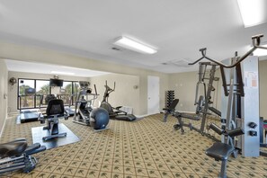 Ein Fitnessraum mit Trainingsgeräten, einem gemusterten Boden und großen Fenstern.