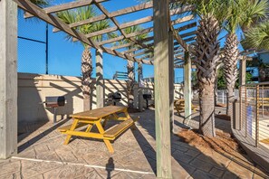 A wooden pergola with a picnic table, surrounded by palm trees and a fenced area. - Walk to Beach🌴 2 Pools + Hot Tub☀️Mainsail 334 (Miramar Beach)