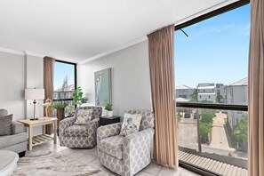 A modern living room with a large window, a sofa set, a side table with a lamp, and a painting on the wall. - Walk to Beach🌴 2 Pools + Hot Tub☀️Mainsail 334 (Miramar Beach)