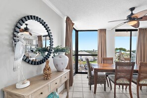 A dining area with a table, chairs, a ceiling fan, and a view through a glass door. - Walk to Beach🌴 2 Pools + Hot Tub☀️Mainsail 334 (Miramar Beach)