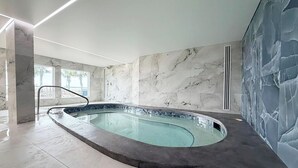 Ein moderner, überdachter Schwimmbereich mit geschwungenem Design, Marmorwänden und einer Glasbarriere.
