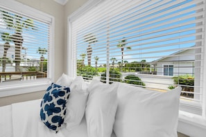 A hotel room with a bed, white bedding, and a view through large windows with blinds. - 🌴Great for Large Groups | Cozy Outdoor Space | Linda's Cozy Collection🏖️ (Panama City Beach)