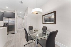 A modern kitchen with stainless steel appliances, a glass dining table with four chairs, and a pendant light. - 3BR Pool Home Near Disney Clermont (Clermont)