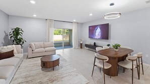 Una sala de estar moderna con un sofá, una mesa de centro, una mesa de comedor, sillas, un televisor y una planta.