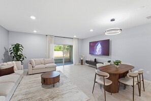 Ein modernes Wohnzimmer mit Sofa, Couchtisch, Esstisch, Stühlen, Fernseher und einer Pflanze.
