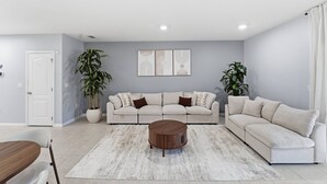 Un salón con un sofá seccional color beige, una mesa de centro redonda y dos plantas en macetas.