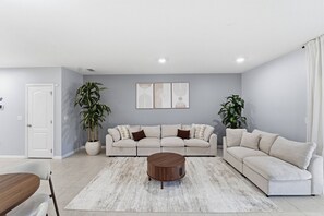 Ein Wohnzimmer mit einem beigefarbenen Ecksofa, einem runden Couchtisch und zwei Blumentöpfen.