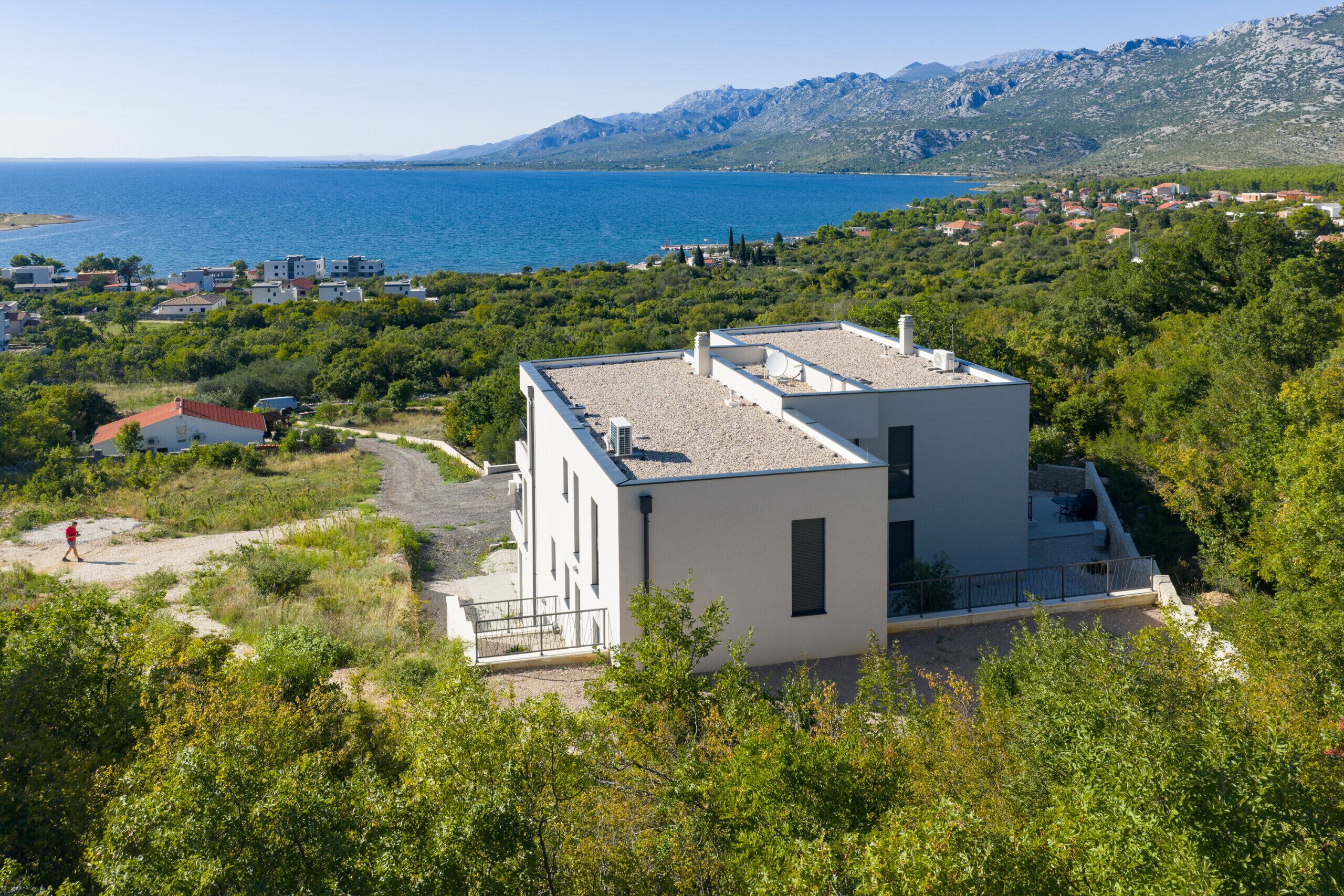 Un edificio moderno con techo plano, rodeado de vegetación y vistas al mar.