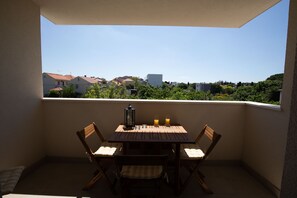 Un balcone con tavolo, sedie e vista su edifici e vegetazione.