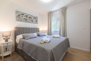 A neatly made bed with a grey quilt, two rolled towels, and a bedside lamp on a white nightstand. - Apartment Klanac 1 with Balcony (Zadar)