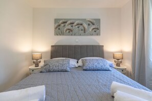 Een netjes opgemaakt bed met een gewatteerde spreidek, twee bedlampjes en een kunstwerk aan de muur erboven.