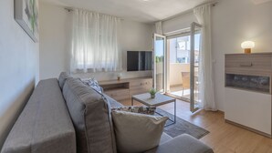 Un salon moderne avec un canapé, un téléviseur et une porte-fenêtre coulissante donnant sur un balcon.