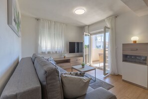 A modern living room with a sofa, TV, and a sliding glass door leading to a balcony. - Apartment Klanac 1 with Balcony (Zadar)