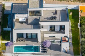 Ein modernes, zweistöckiges Haus mit Dachterrasse, Swimmingpool und angelegtem Garten.