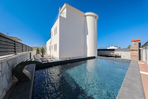 A swimming pool with a stone deck, a white building with a curved corner, and a clear blue sky. - Villa Jimmy with Heated Pool (Starigrad)