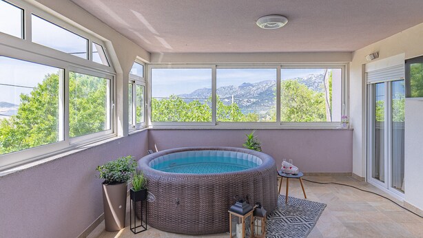 A room with a hot tub, large windows, and a view of mountains. - Apartment Pavao with Whirlpool (Rovanjska)
