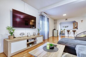 Ein modernes Wohnzimmer mit Fernseher, einem Holzkonsolentisch, einem grauen Sofa und einem Essbereich mit Barhocker.