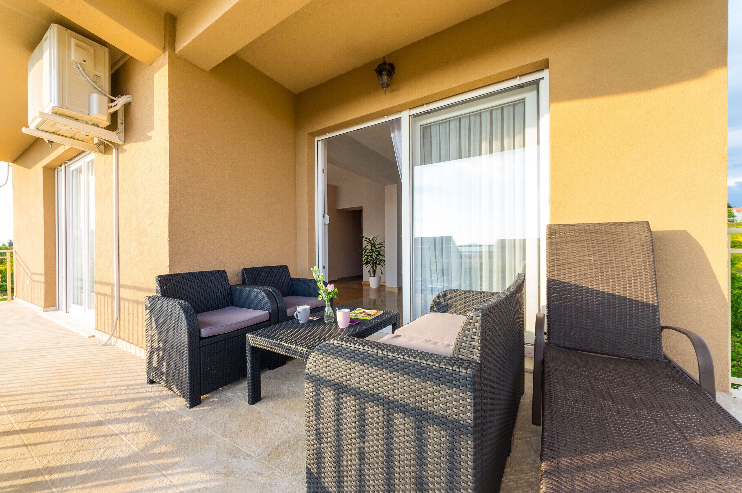 Ein Balkon mit Korbmöbeln, einem Tisch und einem Blumentopf.