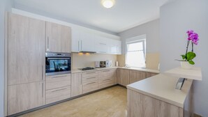 A modern kitchen with light wood cabinets, a built-in oven, and a white countertop. - Apartment Goga 1 with Shared Pool (Zadar)