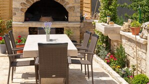 An outdoor patio with a stone fireplace, wicker furniture, and a potted plant. - Apartment Goga 1 with Shared Pool (Zadar)
