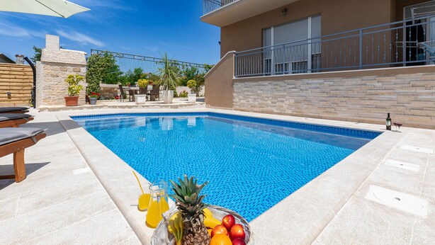 A swimming pool with lounge chairs, a fruit bowl, and a building with balconies. - Apartment Goga 1 with Shared Pool (Zadar)