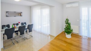 A modern living room with a dining area, a potted plant, and an air conditioning unit. - Apartment Goga 1 with Shared Pool (Zadar)