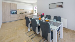 A modern kitchen with white cabinets, a dining area with a glass table and chairs, and a mirror on the wall. - Apartment Goga 1 with Shared Pool (Zadar)