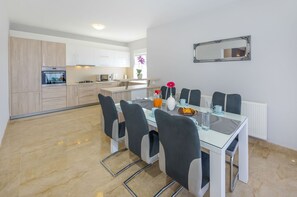 Eine moderne Küche mit weißen Schränken, einem Essbereich mit Glastisch und Stühlen sowie einem Spiegel an der Wand.