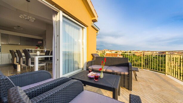 A balcony with wicker furniture, a dining area with chairs and a table, and a view of the cityscape. - Apartment Goga 2 with Shared Pool (Zadar)