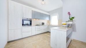 A modern kitchen with white cabinetry, a built-in oven, and a countertop with a coffee maker. - Apartment Goga 2 with Shared Pool (Zadar)