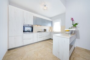 A modern kitchen with white cabinetry, a built-in oven, and a countertop with a coffee maker. - Apartment Goga 2 with Shared Pool (Zadar)