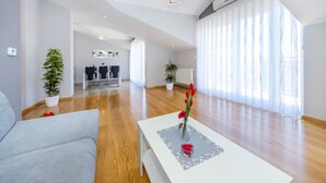 A spacious living room with a white sofa, a coffee table with a vase of flowers, and a dining area in the background. - Apartment Goga 2 with Shared Pool (Zadar)