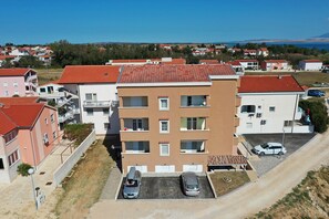 A multi-story residential building with a parking area, a visible balcony, and a clear view of the surrounding neighborhood. - Apartment Sandstrand 4 with Sea View (Nin)
