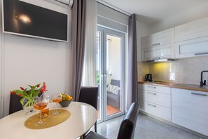 Eine moderne Küche mit Essbereich, einem an der Wand montierten Fernseher und einer Glastür zum Balkon.