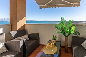 Ein Balkon mit Korbmöbeln, einem Glastisch mit Getränken und einem Blumentopf.