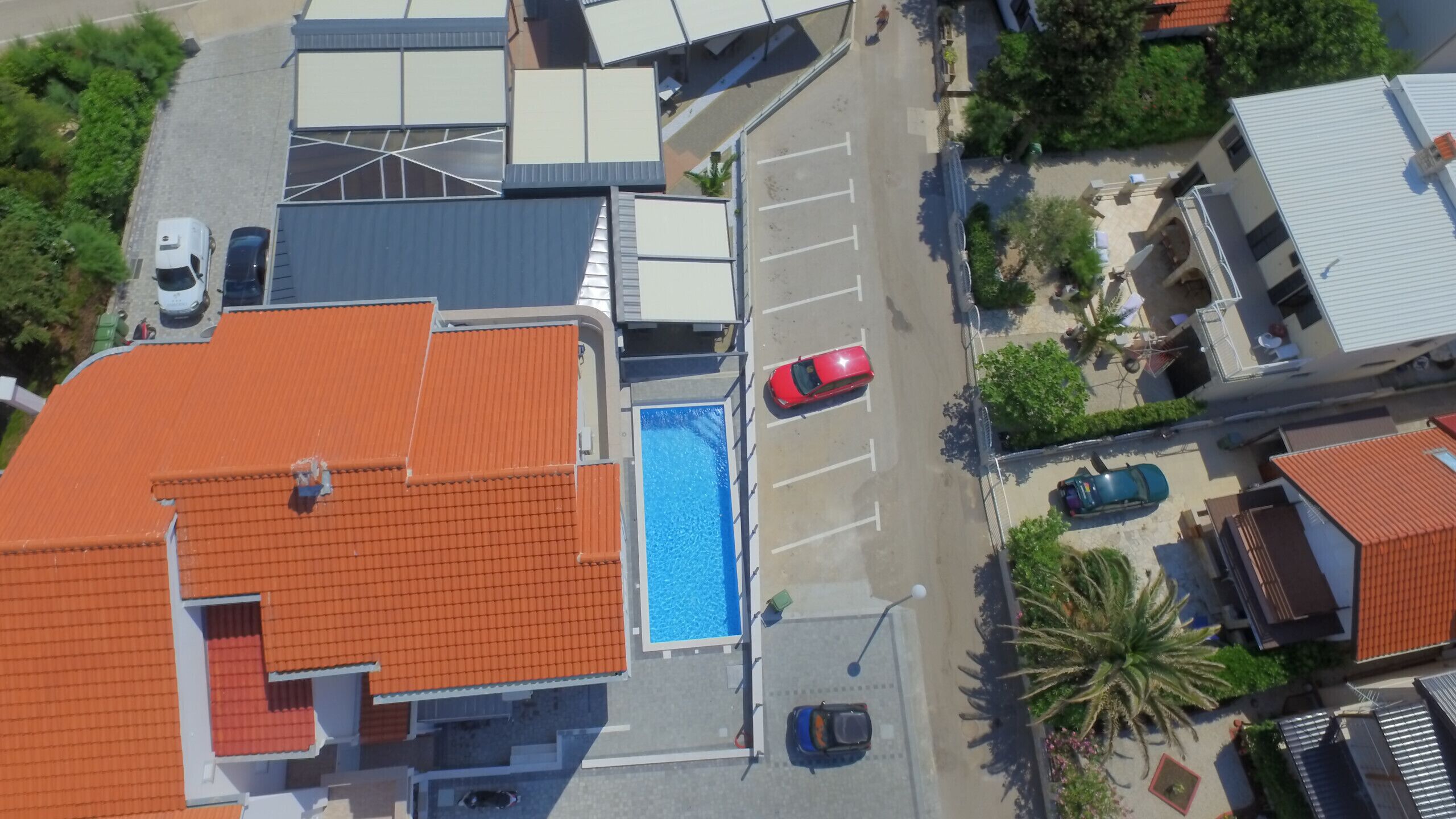 Luchtbeeld van een woongebied met een zwembad, meerdere auto's en een rode auto geparkeerd in de buurt van het zwembad.