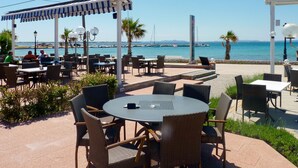 Un área de estar al aire libre con mesas y sillas, una sección cubierta y vistas al mar.