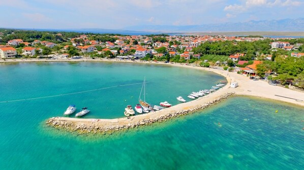 Eine Küstenstadt mit einem Yachthafen, klarem türkisblauem Wasser und Wohnhäusern mit roten Dächern.