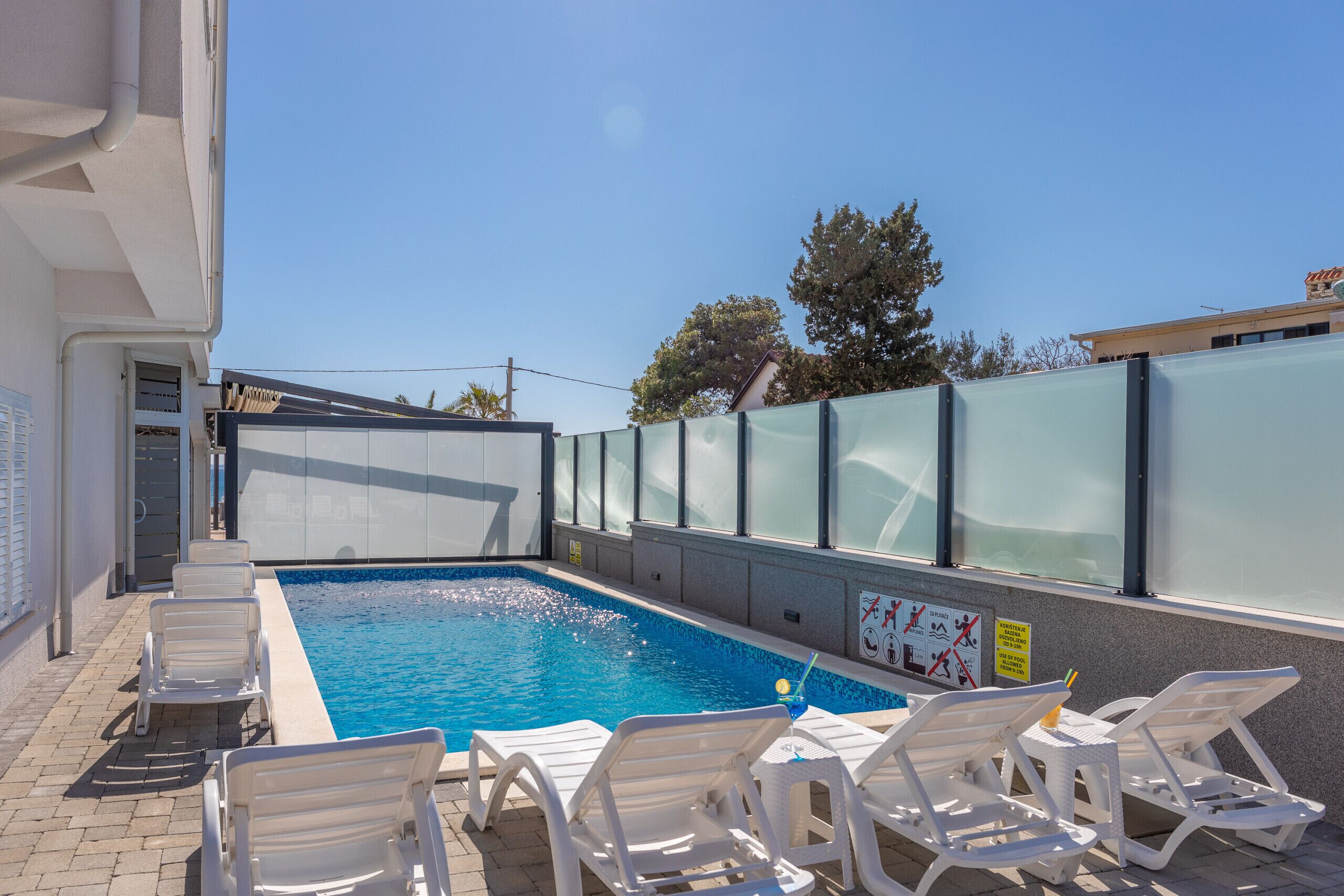 A swimming pool with white lounge chairs, a clear sky, and a building in the background.