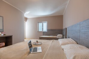 Ein Schlafzimmer mit einem Bett, einem Laptop, einem Nachttisch, einem Fenster und einer kleinen Pflanze.
